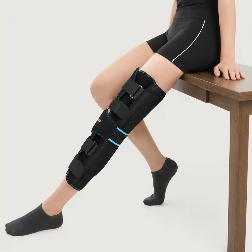 Person wearing a black leg brace on one leg, sitting on a wooden bench.