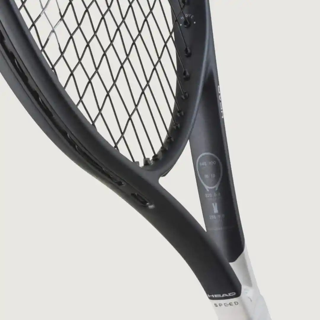 Close-up of a tennis racket showing the black frame, strings, and part of the white grip on a light gray background.