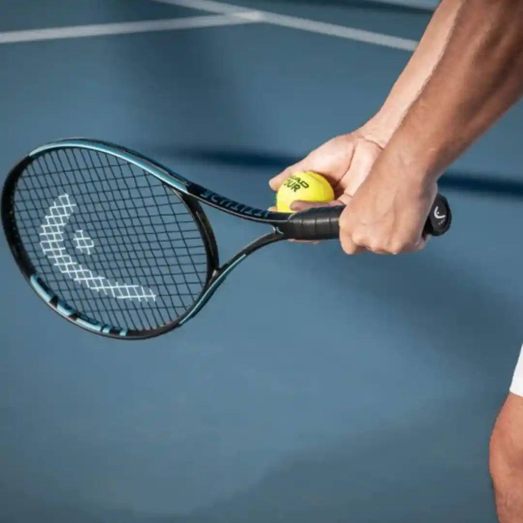 A close-up action shot of a tennis player's hand holding a Wilson tennis racket and a yellow tennis ball on a blue tennis court.