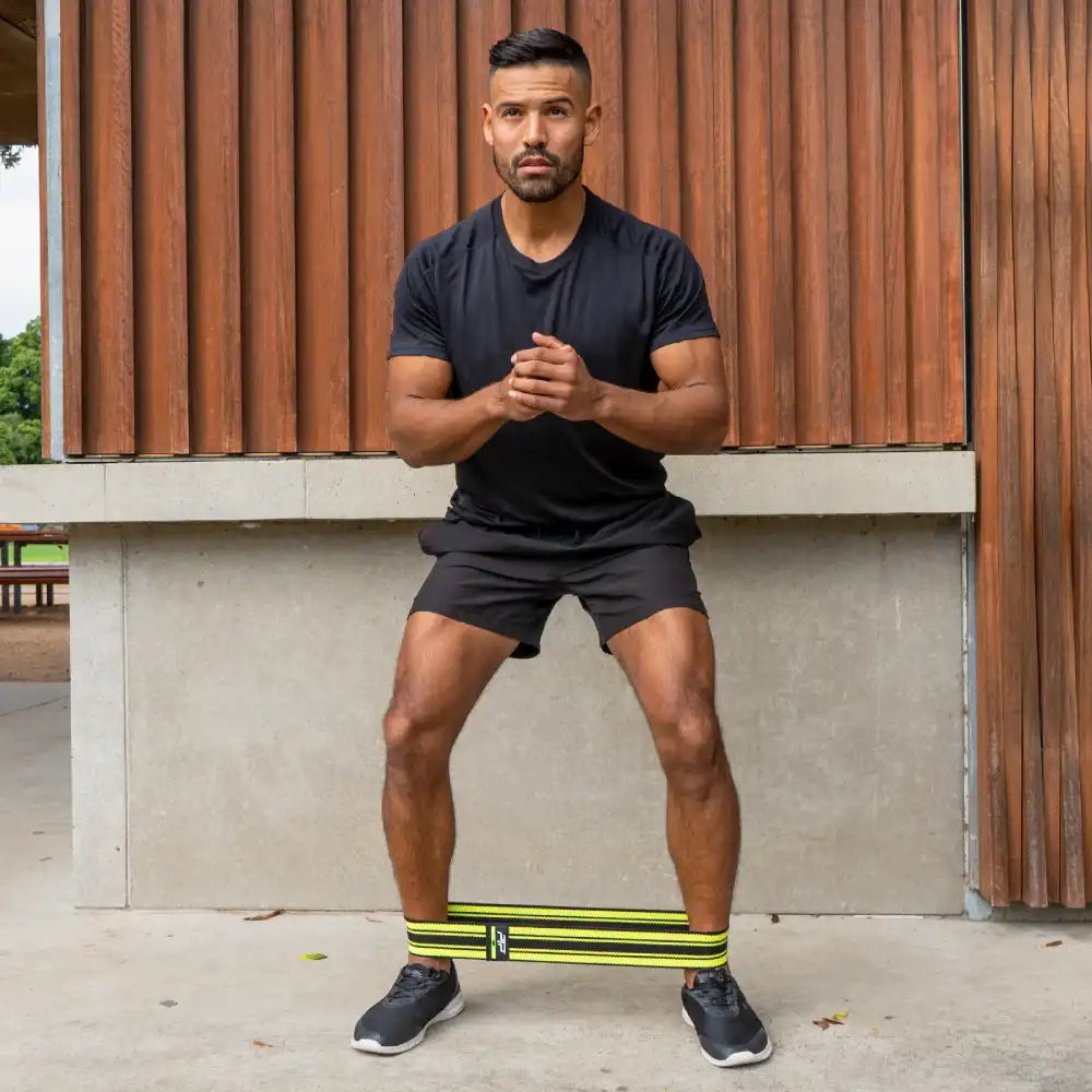 Man in black athletic wear with resistance band standing against a wooden building.