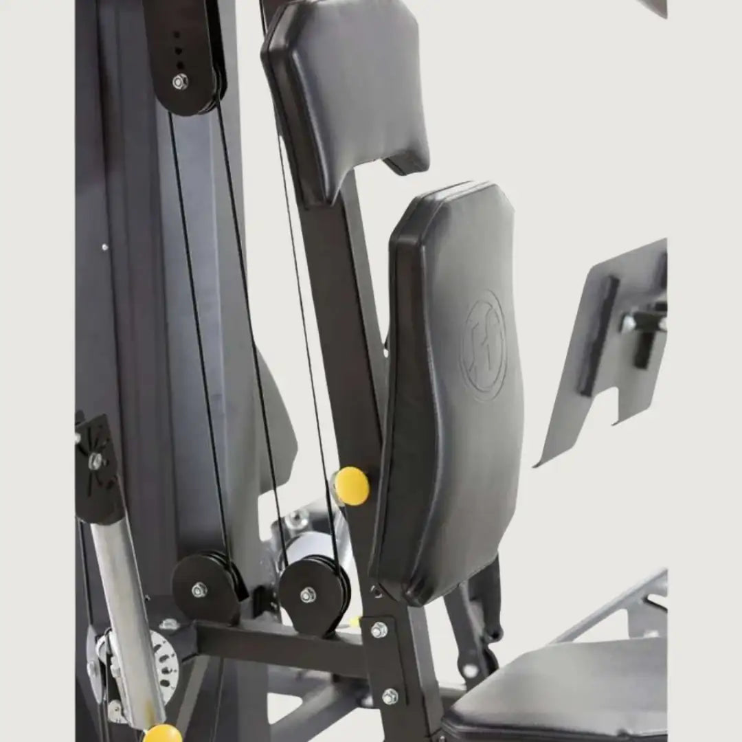 Side angle of the multi-gym highlighting the backrest, shoulder pads, and cable pulleys.